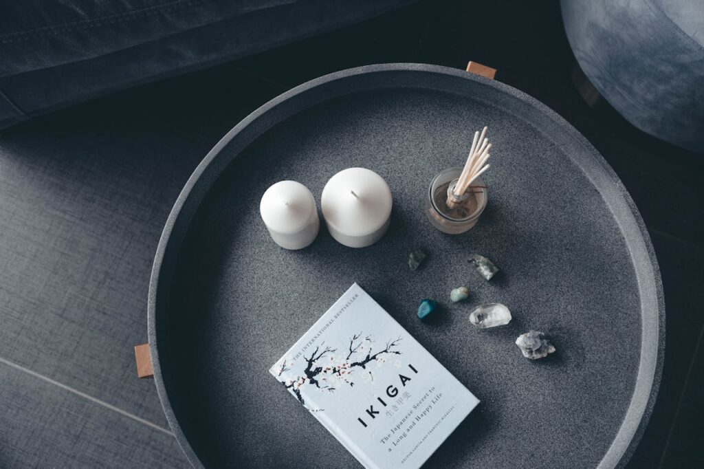 Top view of a serene tabletop setting featuring a book, candles, incense, and gemstones.
